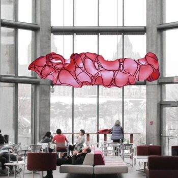 Horizontaal hangend LED Design armatuur in de uitvoering van een roze wolkendek hangend in een hal.